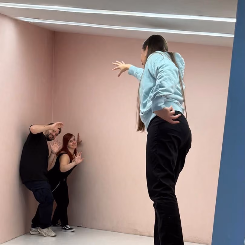 A person appears large reaching out to two smaller people posing worried in a corner of a room.