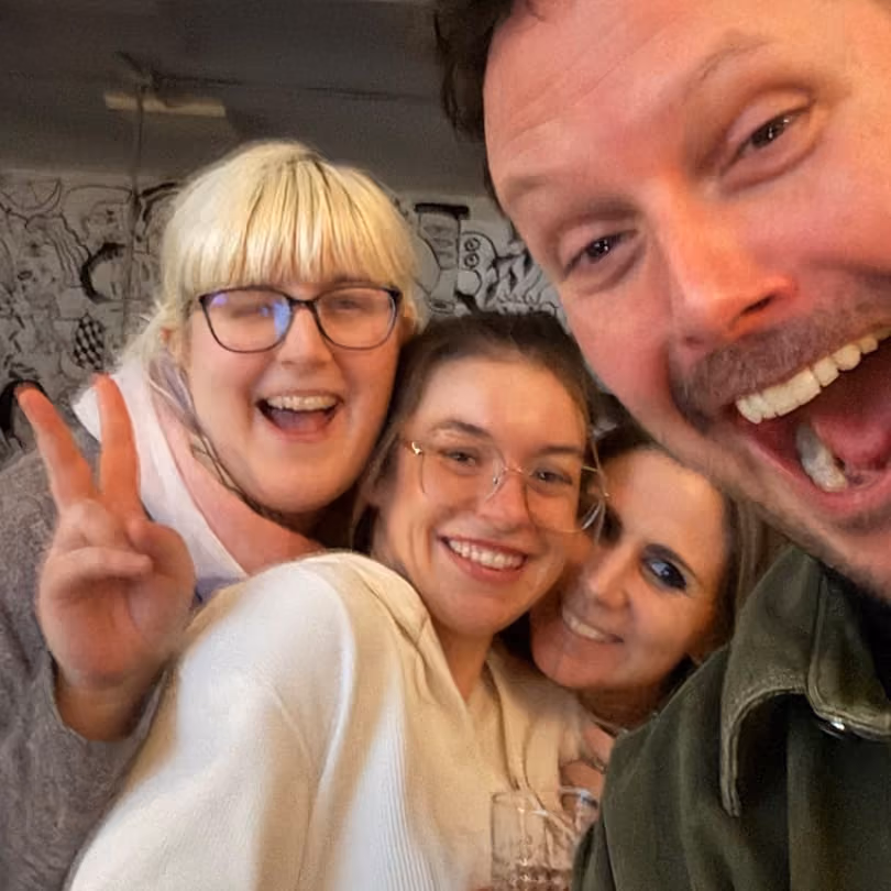 Four happy friends smiling and posing closely for a cheerful group selfie indoors.
