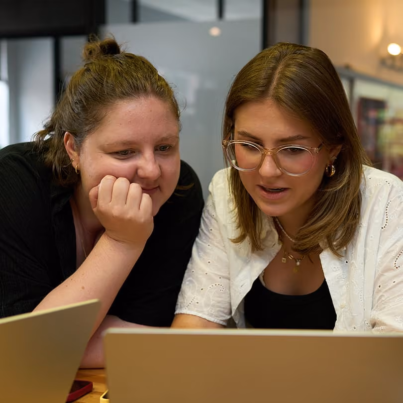 Two women looking intently at a laptop screen, engaged in conversation or work.