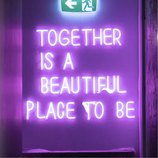 Purple neon sign that reads 'Together is a beautiful place to be' with an emergency exit sign above it.
