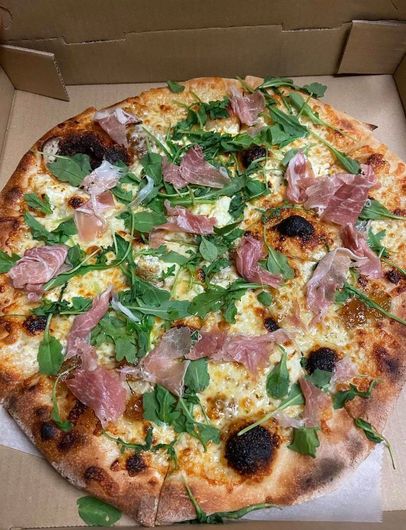A pizza with meat and greens on top.