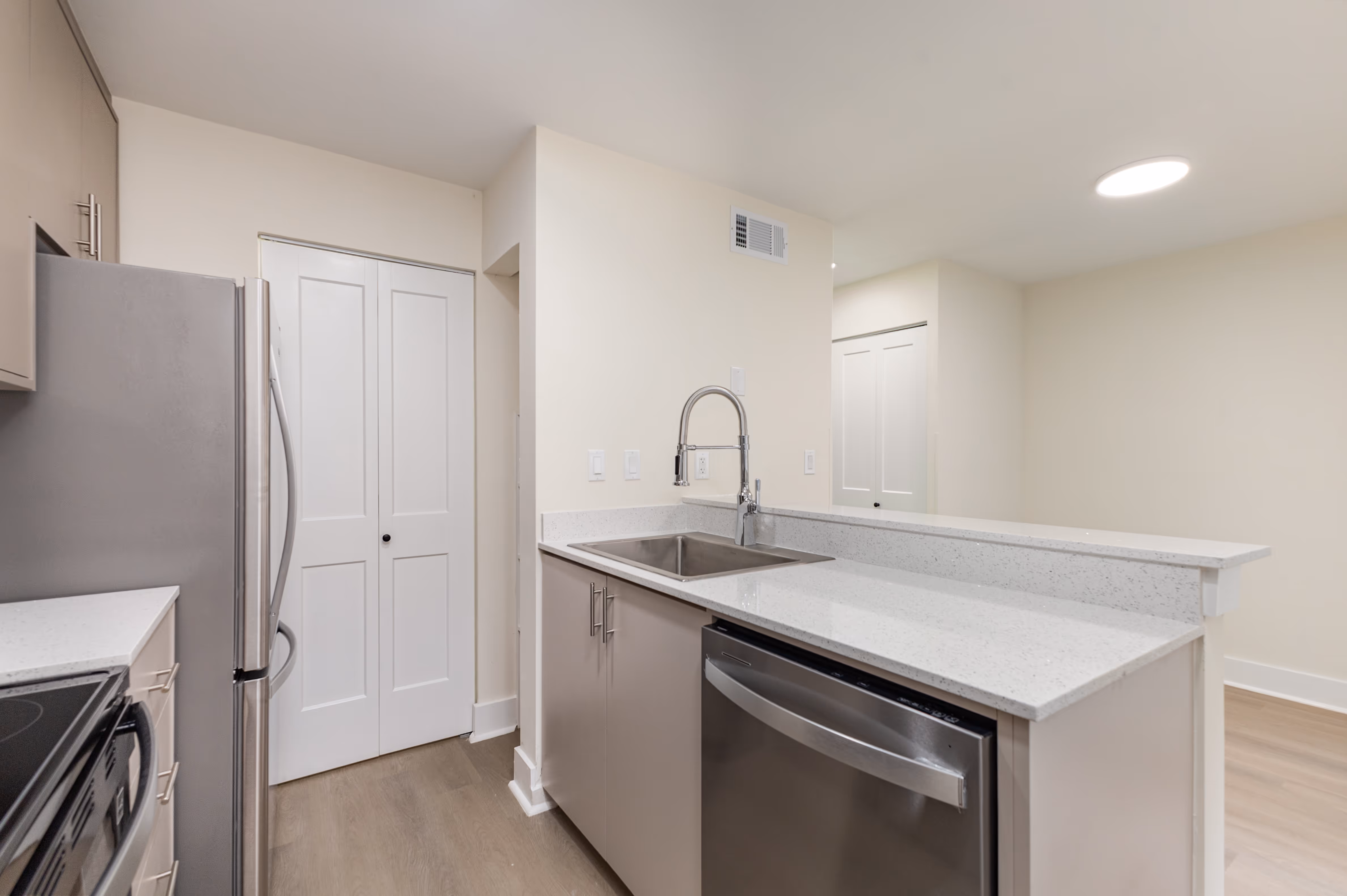 Modern kitchen with stainless steel refrigerator, sink with high-arc faucet, dishwasher, light beige cabinets, and white quartz countertops.