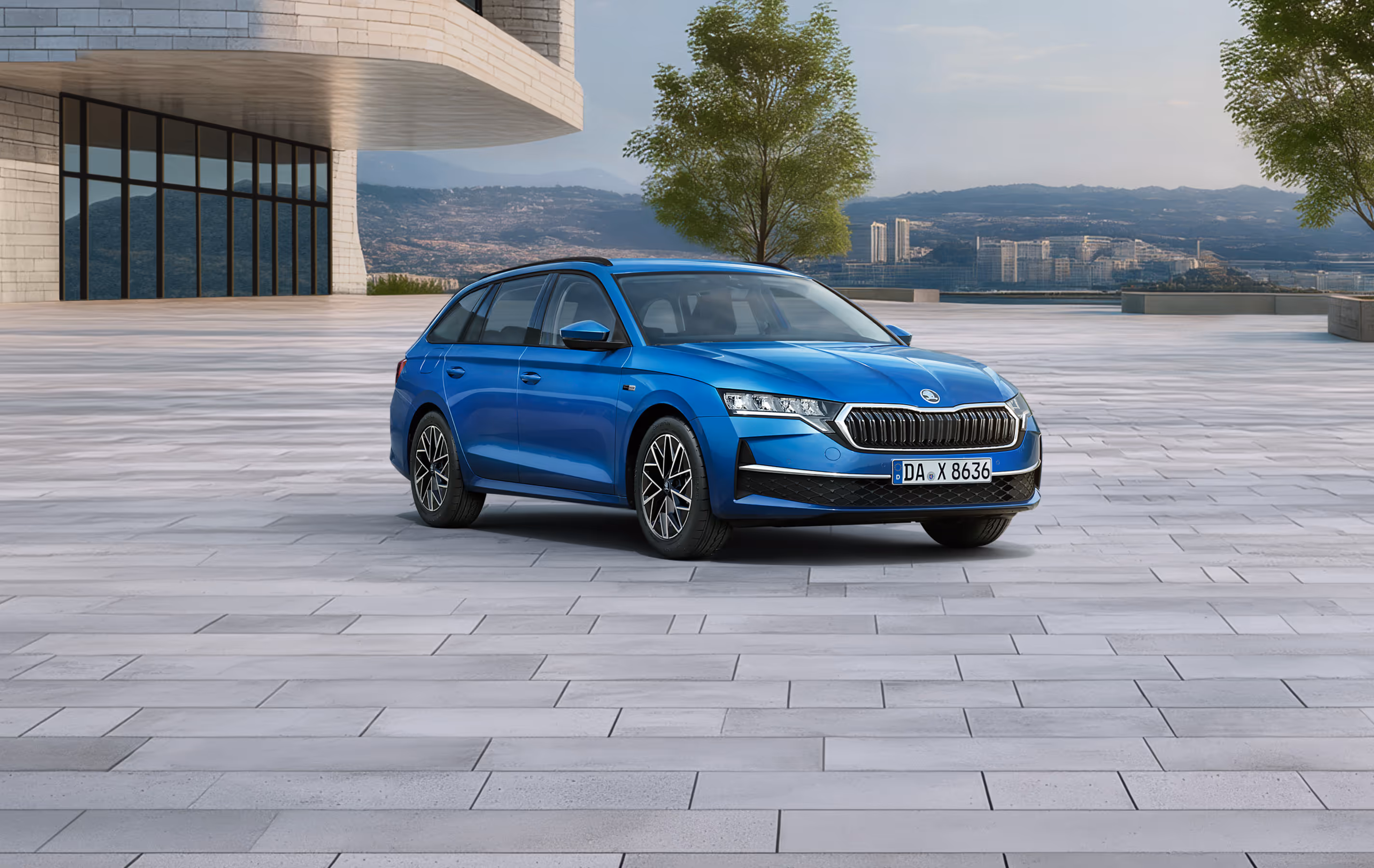 Das Bild zeigt das Balance-Sondermodell Škoda Octavia Combi in der Farbe Race-Blau Metallic aus der vorderen linken schrägen Perspektive auf einem weitläufigen, gepflasterten Platz vor einer Stadtkulisse. Zu sehen sind Exterieur-Details wie die silbernen Leichtmetallfelgen, der Kühlergrill mit Chromrahmen sowie die schwarze Dachreling. Am unteren linken Bildrand hebt ein hellgrüner Störer einen Preisvorteil sowie die inkludierte 5-Jahres-Garantie hervor.