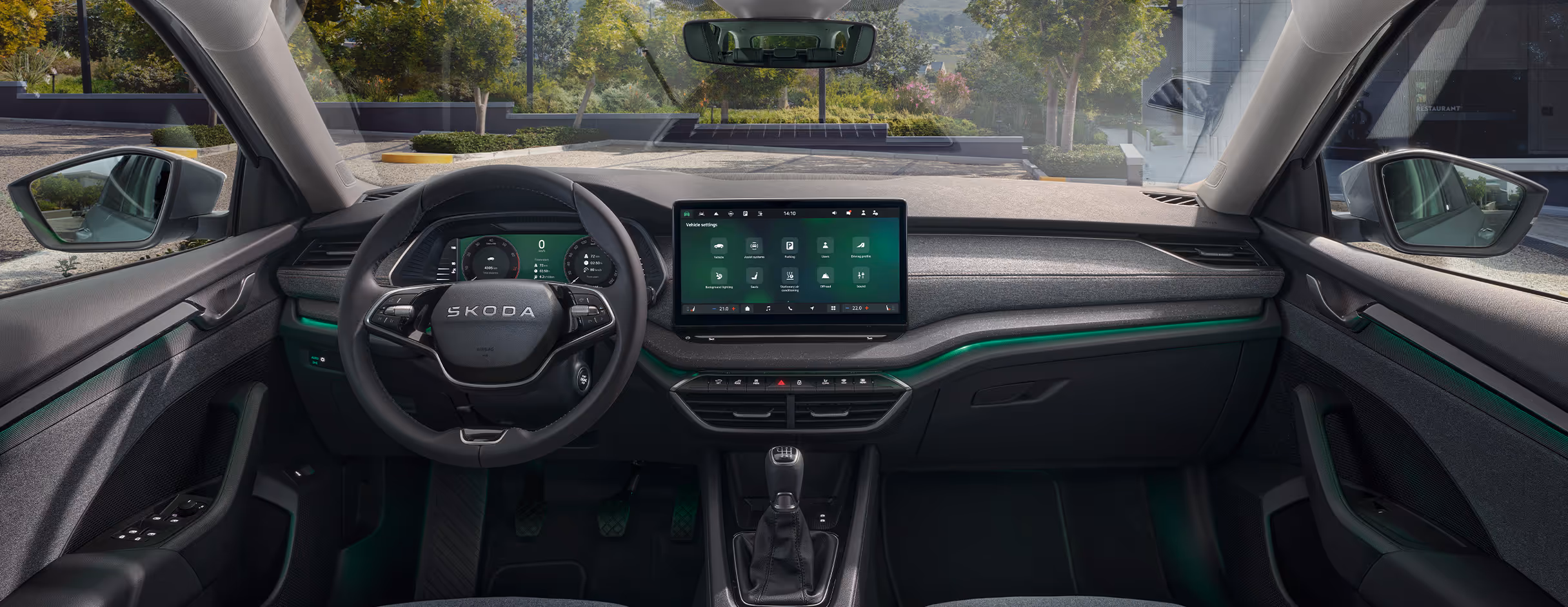 Das Bild zeigt den Innenraum des Škoda Octavia Balance aus der Fahrerperspektive mit Blick auf das Armaturenbrett und durch die Frontscheibe nach draußen. Zu den zentralen Elementen gehören das Zweispeichen-Multifunktionslenkrad, das digitale Kombiinstrument sowie der freistehende Infotainment-Touchscreen. Grüne Plus-Symbole heben interaktive Bereiche hervor, darunter das Infotainment-Display, die Phonebox sowie die Ambientebeleuchtung. 