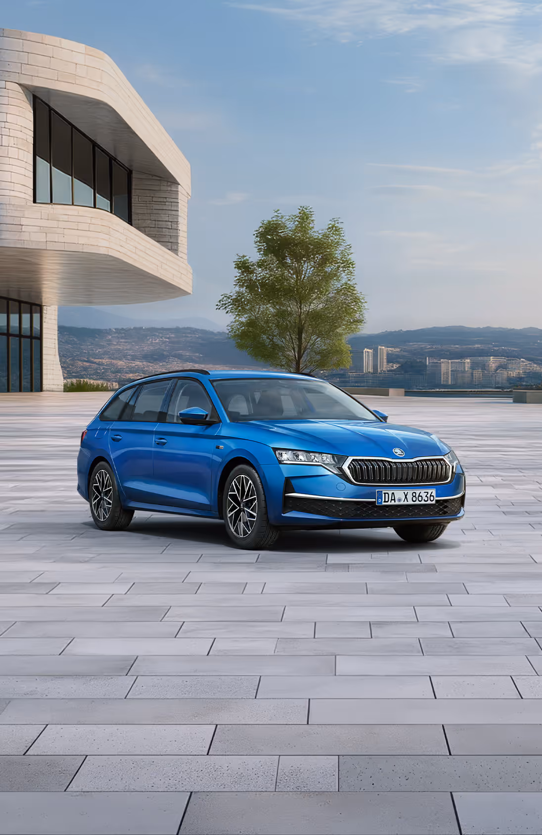 Das Bild zeigt das Balance-Sondermodell Škoda Octavia Combi in der Farbe Race-Blau Metallic aus der vorderen linken schrägen Perspektive auf einem weitläufigen, gepflasterten Platz vor einer Stadtkulisse. Zu sehen sind Exterieur-Details wie die silbernen Leichtmetallfelgen, der Kühlergrill mit Chromrahmen sowie die schwarze Dachreling. Am unteren linken Bildrand hebt ein hellgrüner Störer einen Preisvorteil sowie die inkludierte 5-Jahres-Garantie hervor.