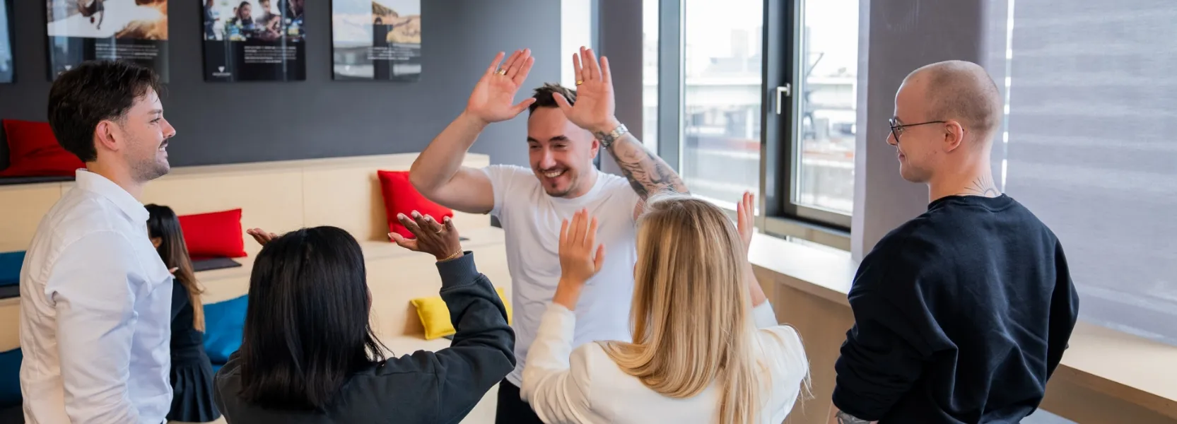 Fünf Kollegen in einem modernen Büro geben sich lachend High-Fives und wirken motiviert.