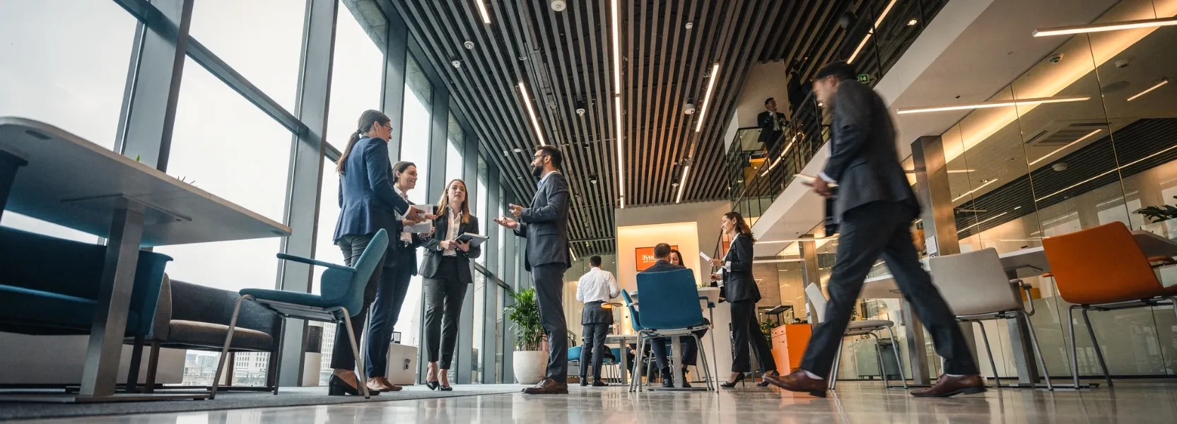 Geschäftsleute in einem modernen Bürogebäude mit großen Fenstern führen Gespräche und arbeiten gemeinsam.