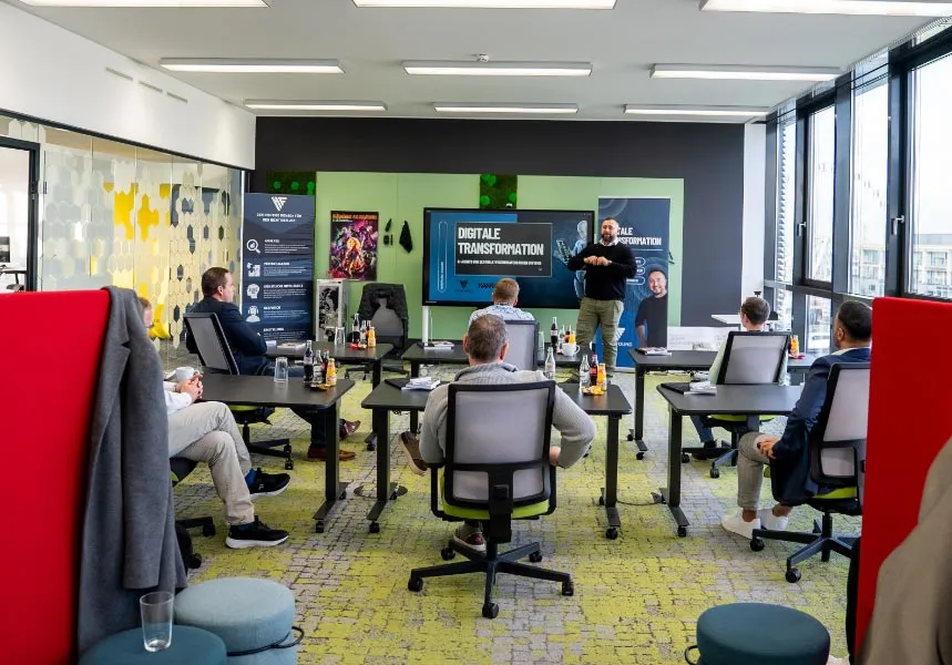 Ein Mitarbeiter hält einen Vortrag über digitale Transformation vor sechs Teilnehmern in einem modernen Büro mit großen Fenstern.