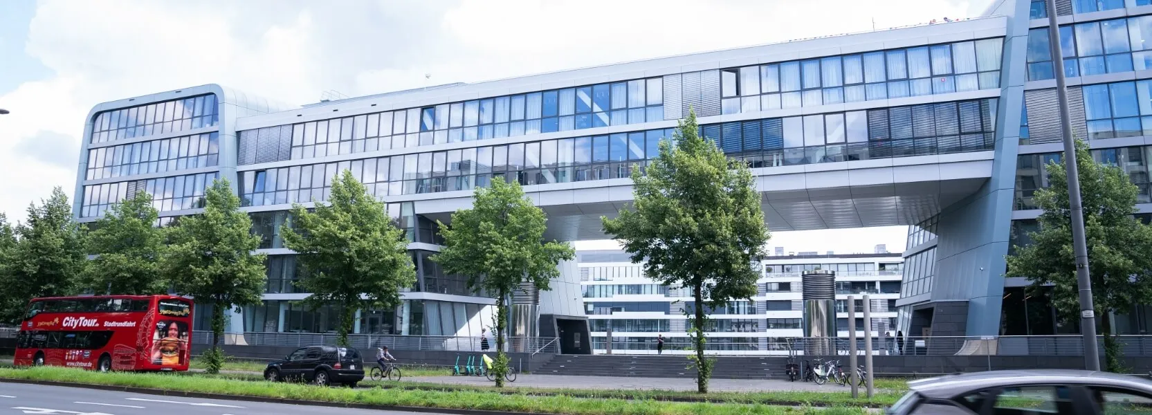 Microsoft Bürogebäude in Köln mit großer, überdachter Freitreppe, Bäumen im Vordergrund und einem roten Doppeldecker-Bus.