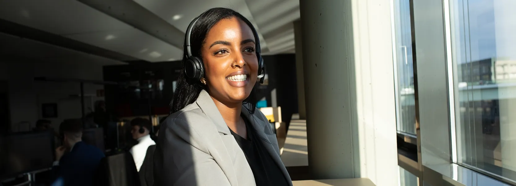 Mann mit Kopfhörern hält einen Stift und blickt konzentriert in Richtung eines Computers in einem Büro.