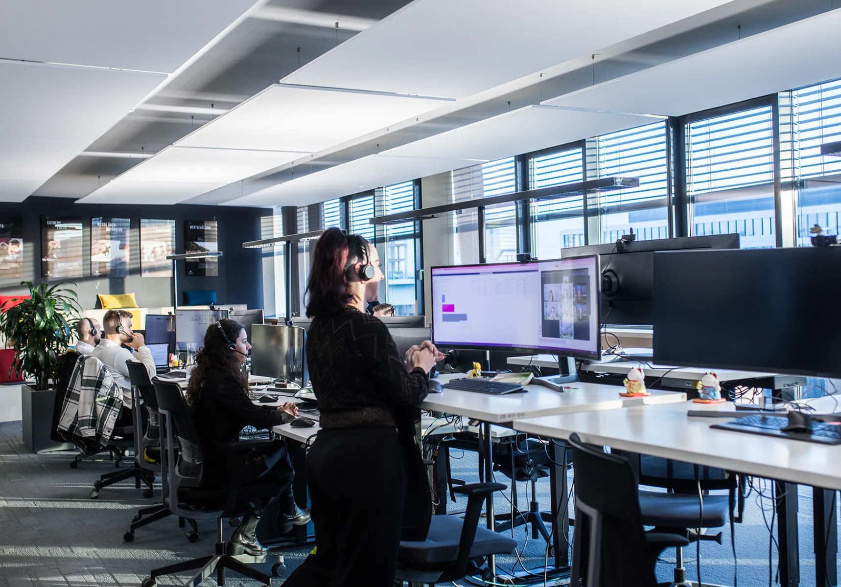 Büroumgebung mit mehreren Personen, die an Schreibtischen mit Computern arbeiten.