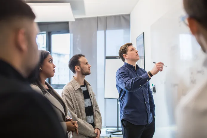 Ein Mitarbeiter hält einen Vortrag über digitale Transformation vor sechs Teilnehmern in einem modernen Büro mit großen Fenstern.