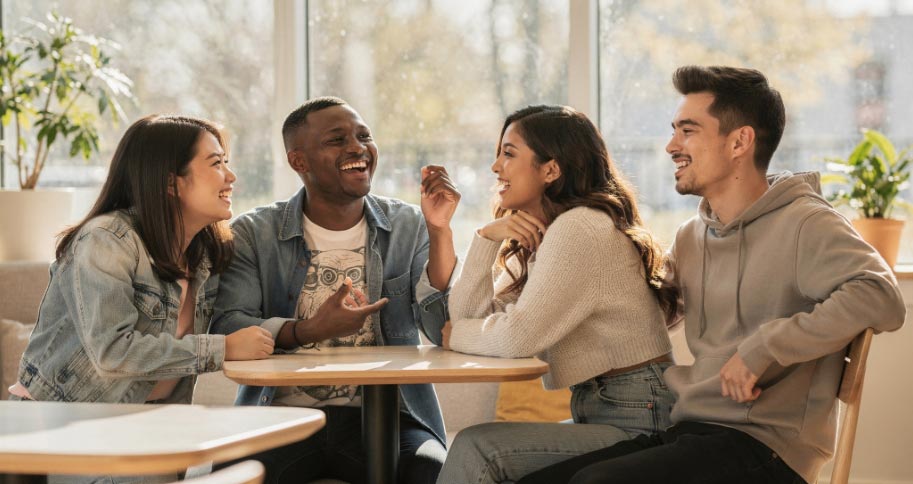 Diverse Gruppe junger Erwachsener teilt einen fröhlichen Moment in entspannter Café-Atmosphäre.