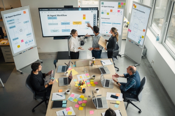 Eine Gruppe von Personen sitzt in einem Büro und diskutiert über Informationen auf Flipcharts.