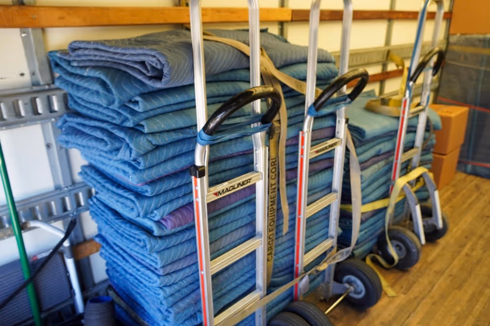 Hand trucks and stacked blue moving blankets for secure packing by long distance movers in Austin, TX.