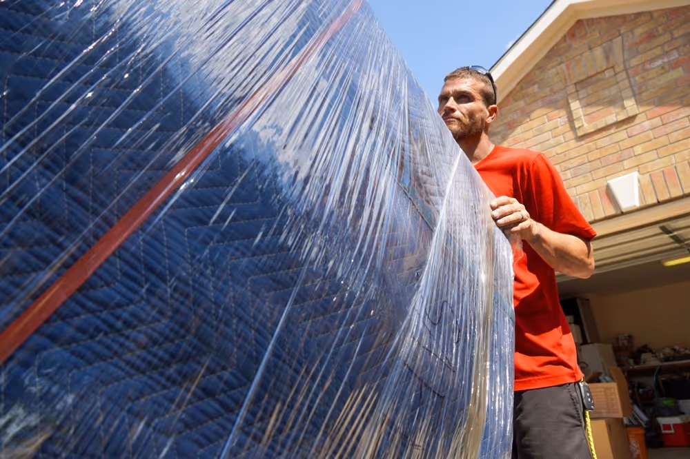 Austin long distance movers securely wrapping and moving furniture with protective blankets and plastic wrap for transit.