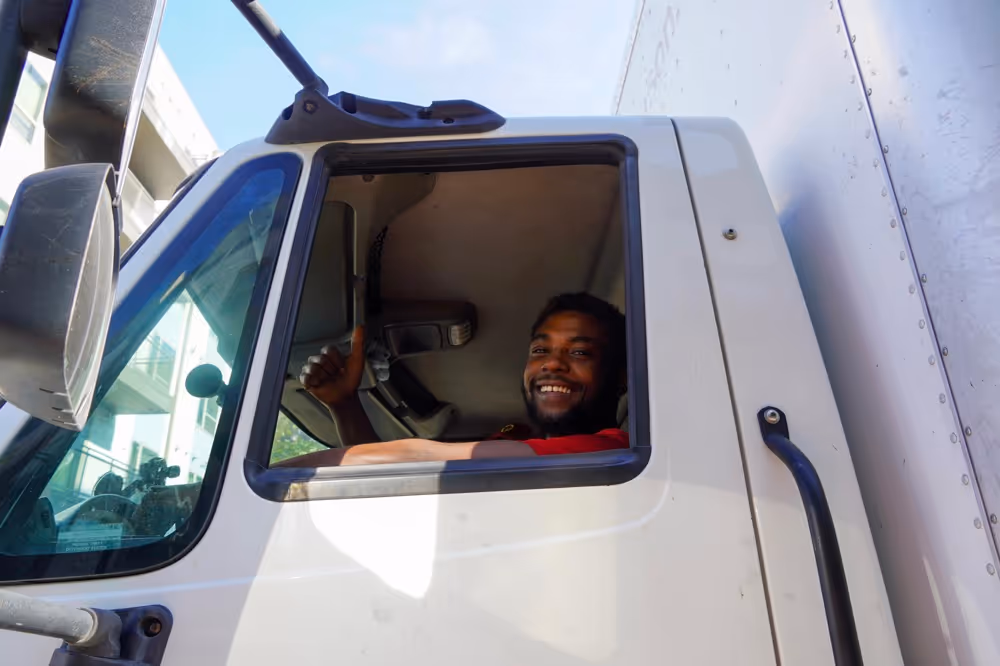 Close-up of a happy interstate moving company driver in Austin, TX, giving a thumbs-up from the window of a commercial moving truck.