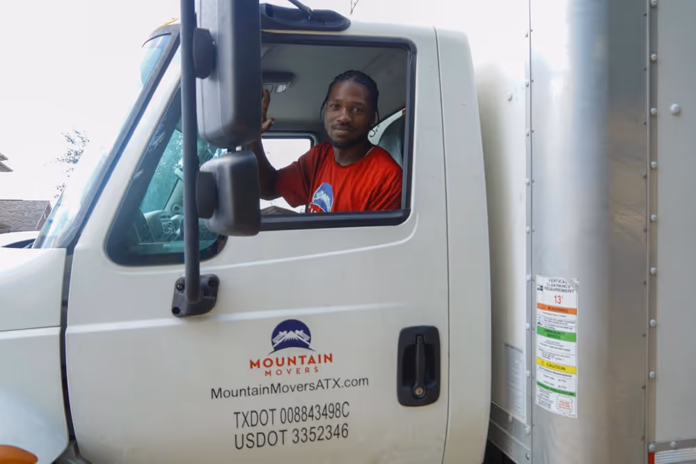Moving truck cab with "Mountain Movers ATX" logo and TXDOT/USDOT numbers clearly visible, featuring a mover looking out the window, emphasizing legal and reliable interstate moving in Austin.