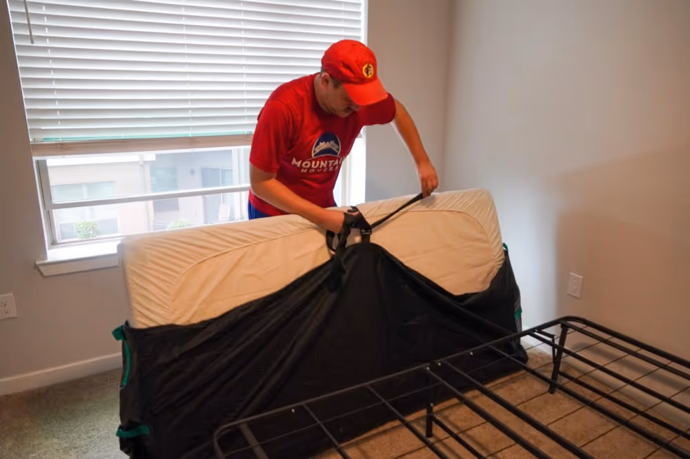 Professional Austin TX mover securing mattress with protective cover and strap inside apartment bedroom.