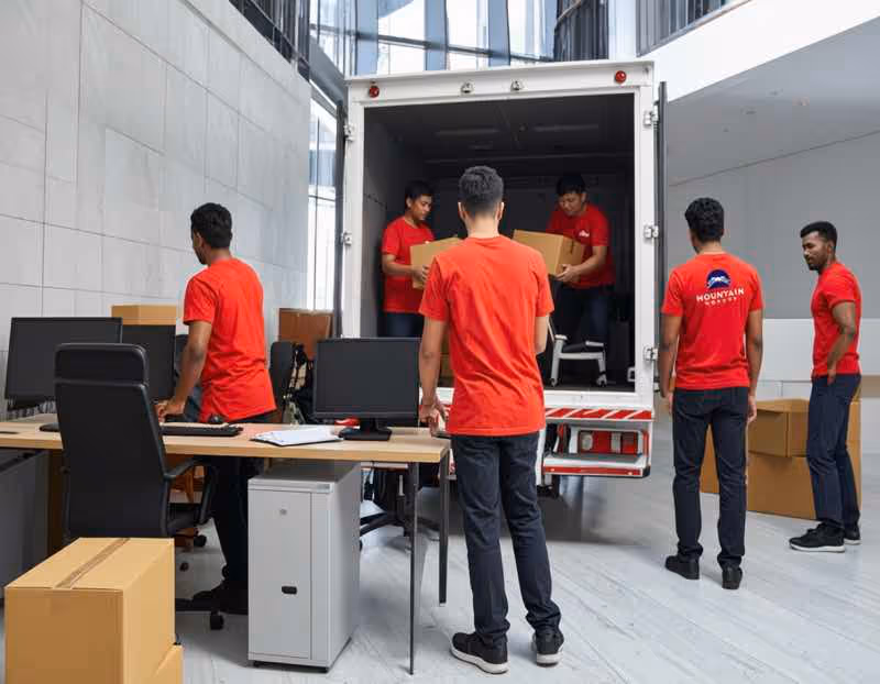 Moving crew loading boxes from a corporate office space into the back of a moving truck, with a visible Mountain Movers logo on a crew member's shirt. Keywords: office moving services Austin TX, commercial moving crew, large corporate move.