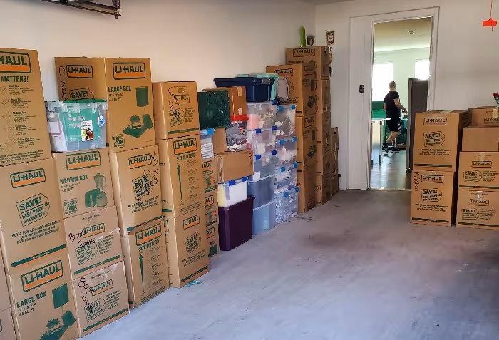 Large collection of stacked U-Haul moving boxes, various plastic totes, and household items packed in a garage, ready for loading and long-distance moving.