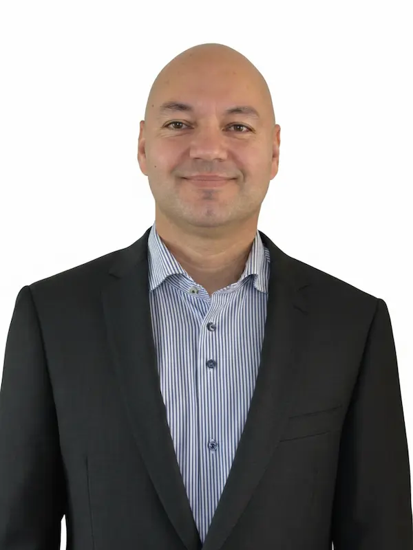 Uw adviseur, Roy Bekkink, draagt een zwart pak en een blauw-wit gestreept overhemd en glimlacht.