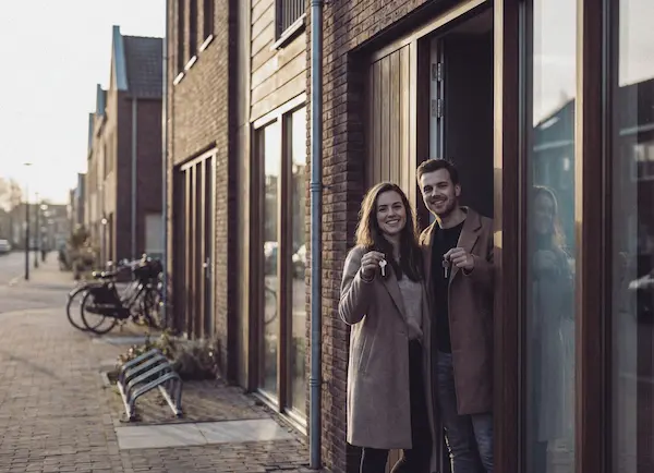 Vrolijk koppel staat in de deuropening van een nieuw huis en houdt sleutels omhoog.