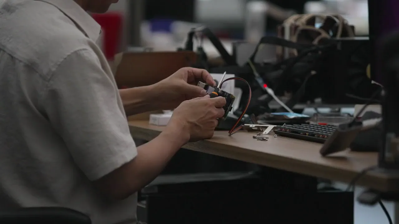 Person working on electronic components at a cluttered desk with tools and a keyboard.