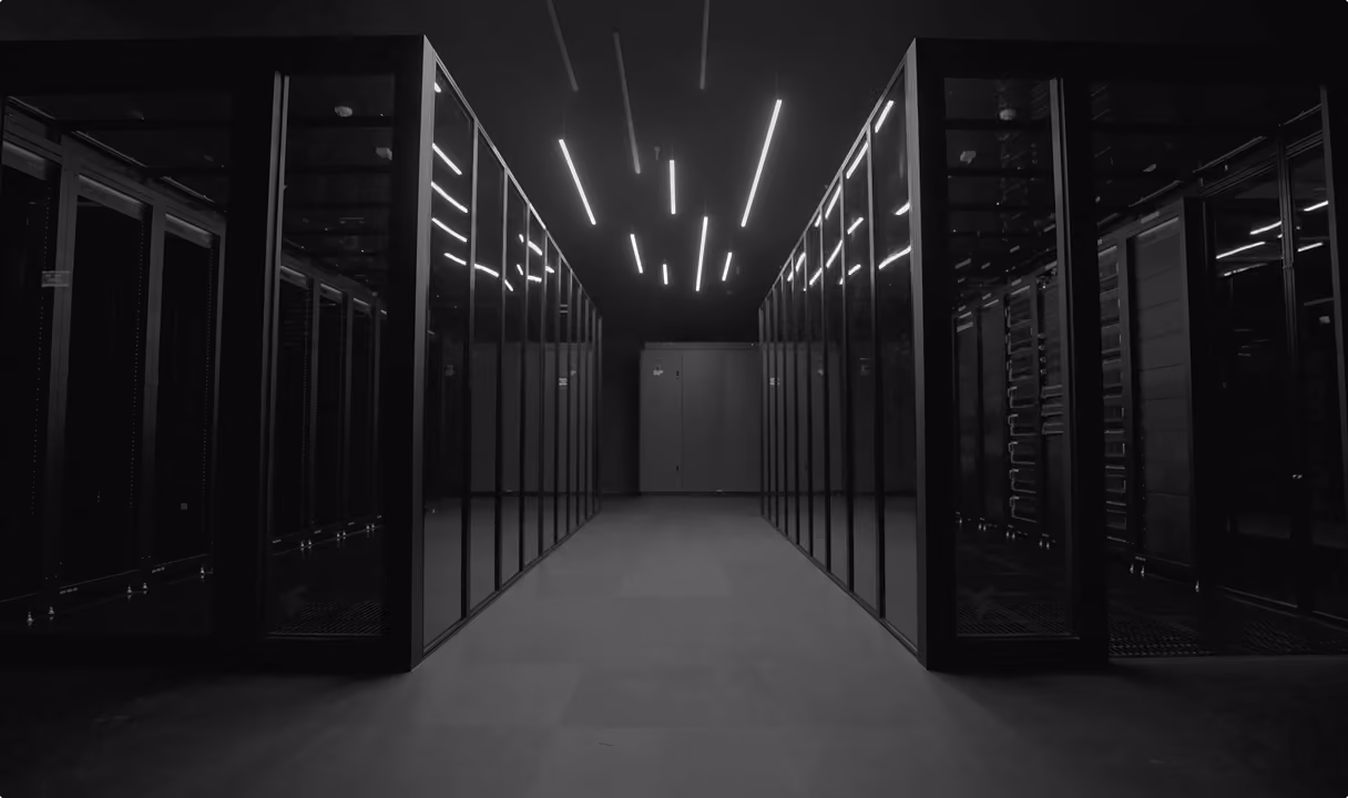 Dimly lit data center aisle with rows of black server racks on both sides and linear ceiling lights.