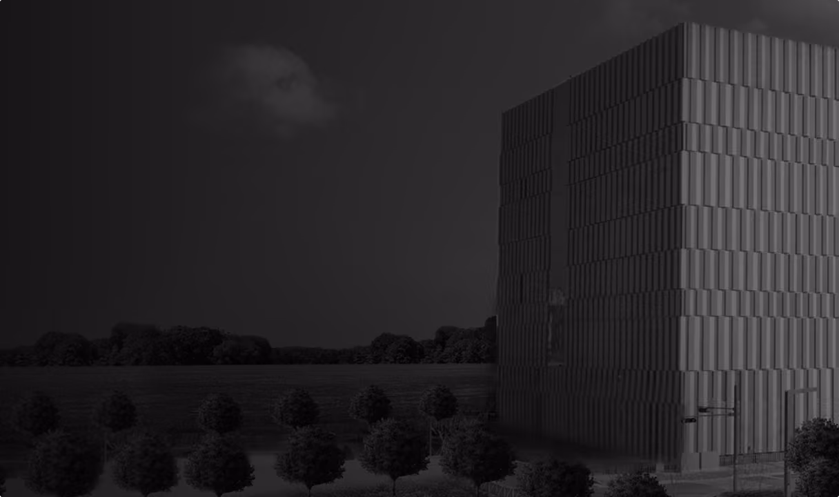 Modern cubic building with a patterned facade stands in a landscaped area with rows of trees and a cloudy sky in the background.