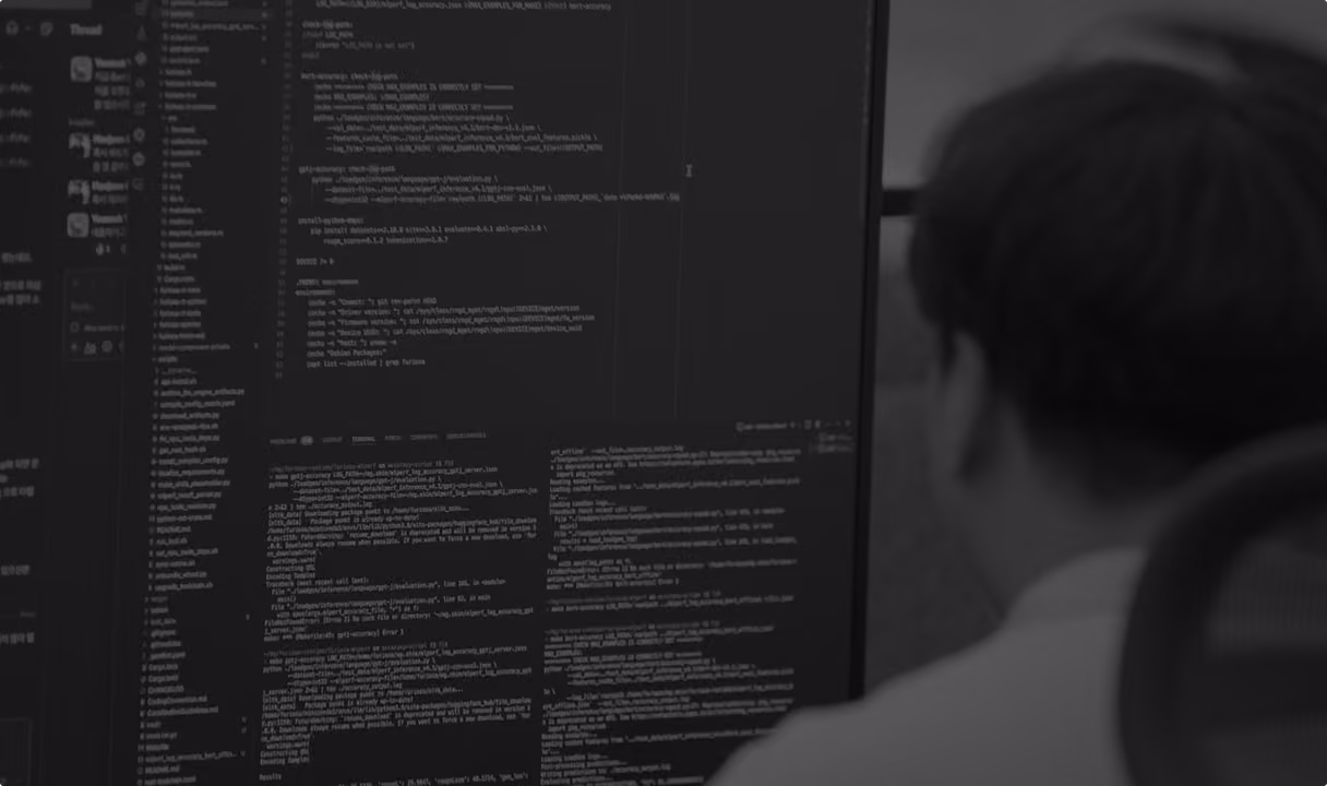 Person with brown hair, viewed from behind, sitting in front of a large computer screen filled with dense programming code and file directories.