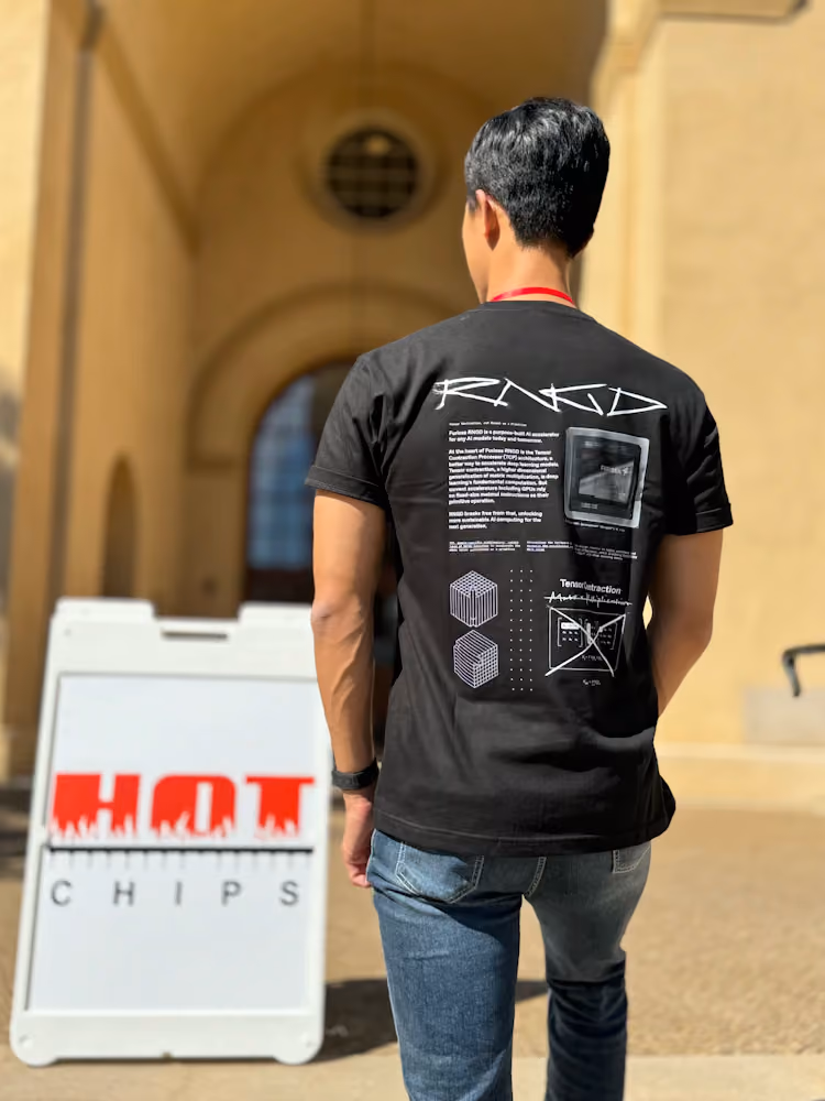 Person wearing a black Furiosa RNGD T-shirt seen from behind, walking toward a building entrance, with a “Hot Chips” conference sign in the foreground, highlighting Furiosa’s presence at a semiconductor and AI hardware event.