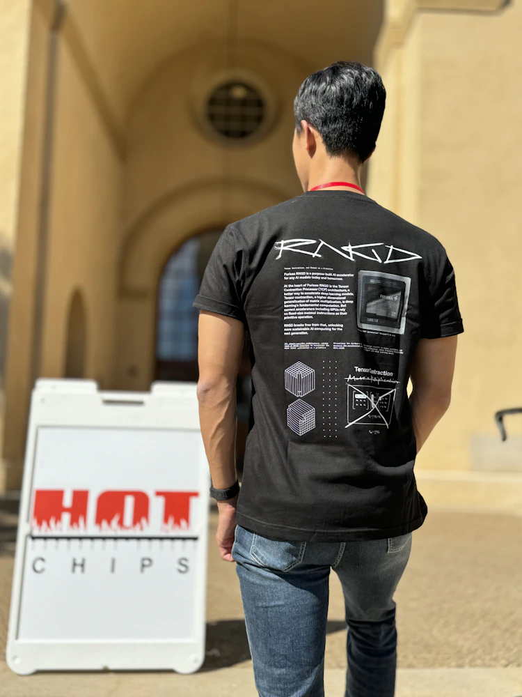 Person wearing a black Furiosa RNGD T-shirt stands outdoors near a sign reading “Hot Chips,” with technical graphics and text printed on the back of the shirt.