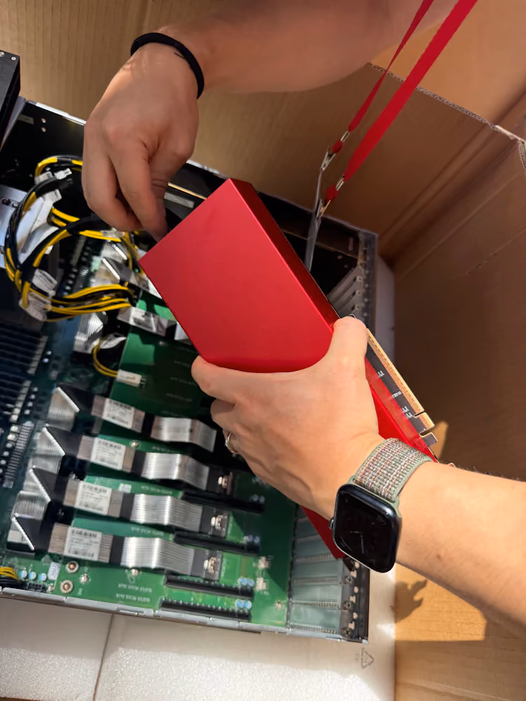Hands installing a red Furiosa RNGD accelerator card into an open server chassis, with visible cabling, PCIe slots, and internal components during hardware setup or assembly.
