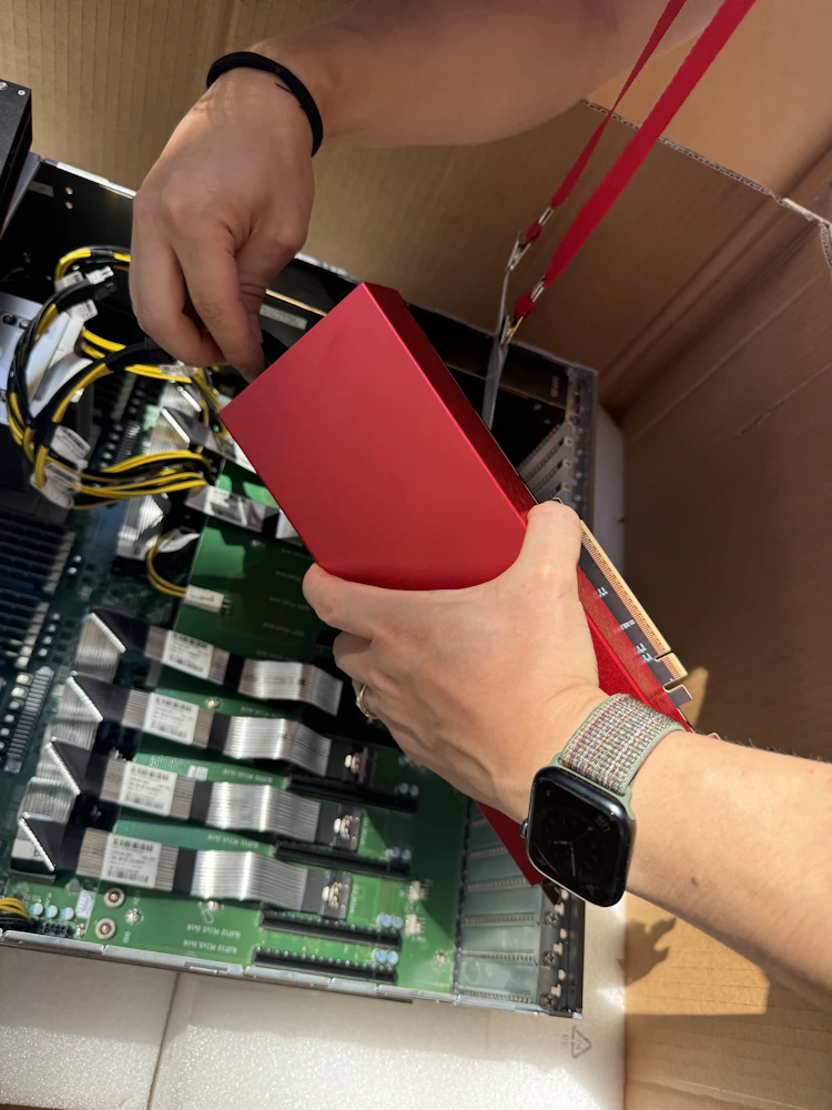 Hands installing a red Furiosa RNGD accelerator card into an open server chassis, with visible cabling, PCIe slots, and internal components during hardware setup or assembly.