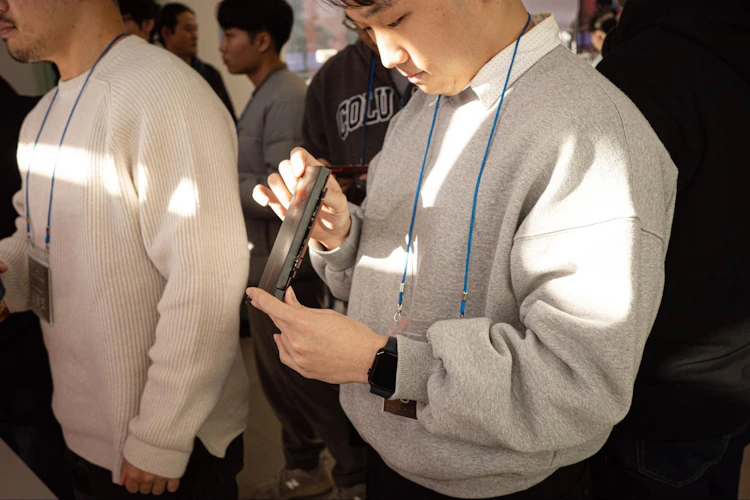 A hackathon attendee closely examines a FuriosaAI accelerator card in their hands, surrounded by other participants wearing badges in a crowded indoor event space.