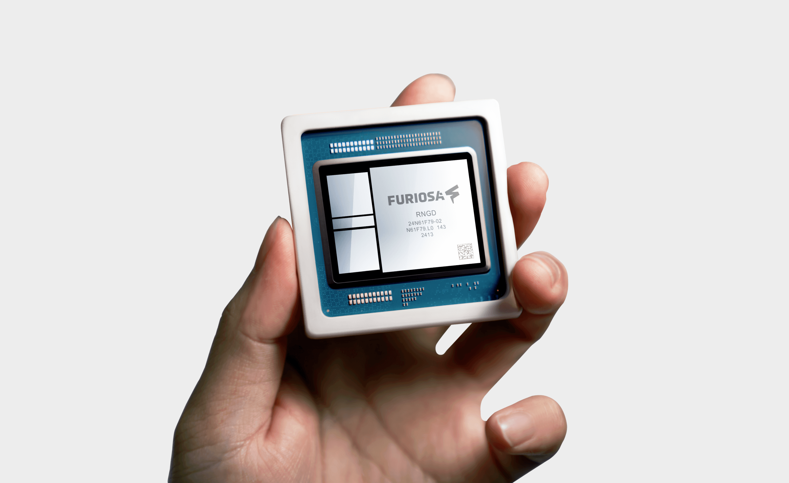 Hand holding a Furiosa RNGD AI processor chip, showing the labeled semiconductor package and exposed die, isolated against a light background.