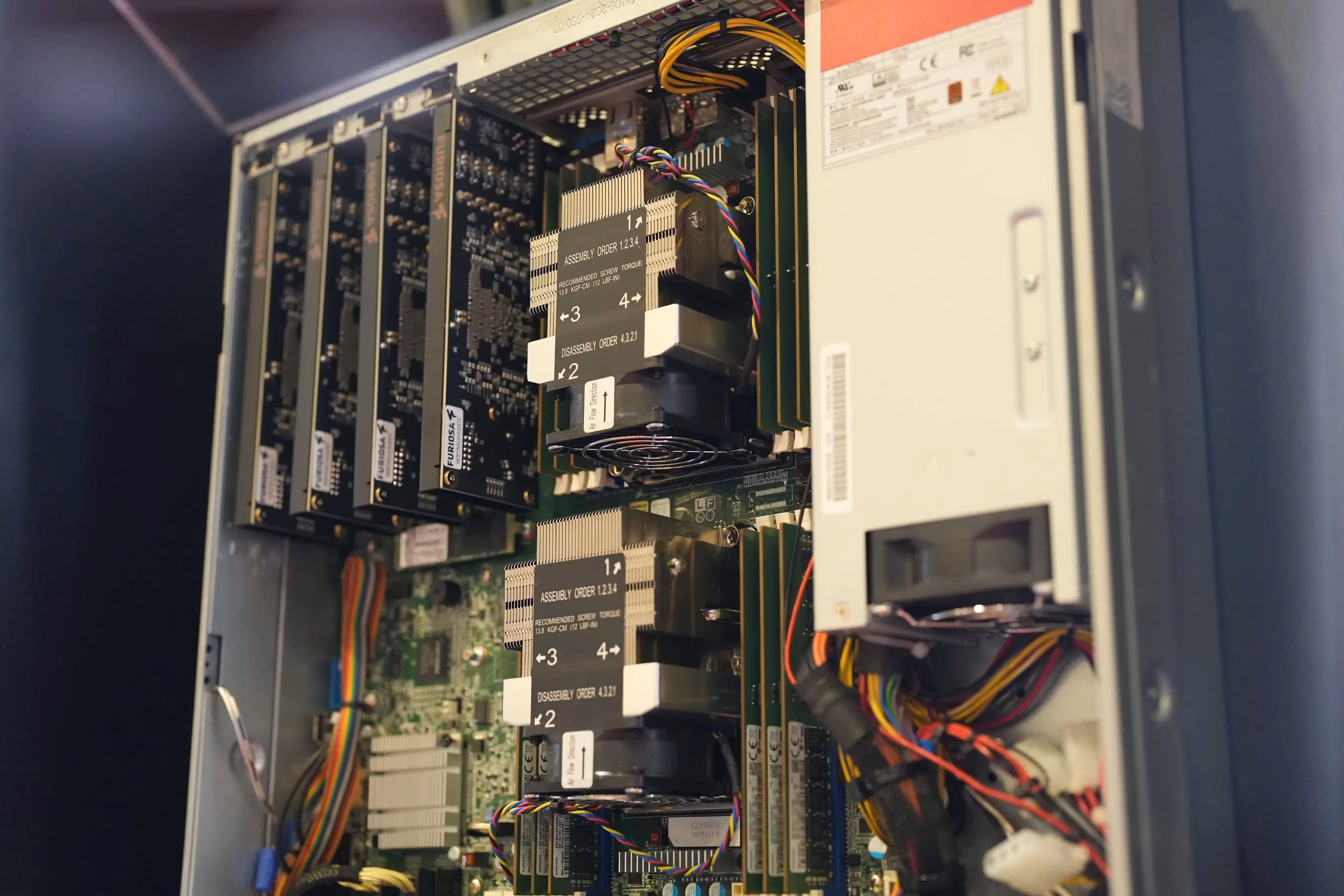 Close-up view inside a server chassis showing multiple accelerator cards installed vertically alongside large heatsinks, cooling fans, memory modules, and bundled power cables. The image highlights the internal hardware layout of a high-performance AI computing system designed for intensive workloads.