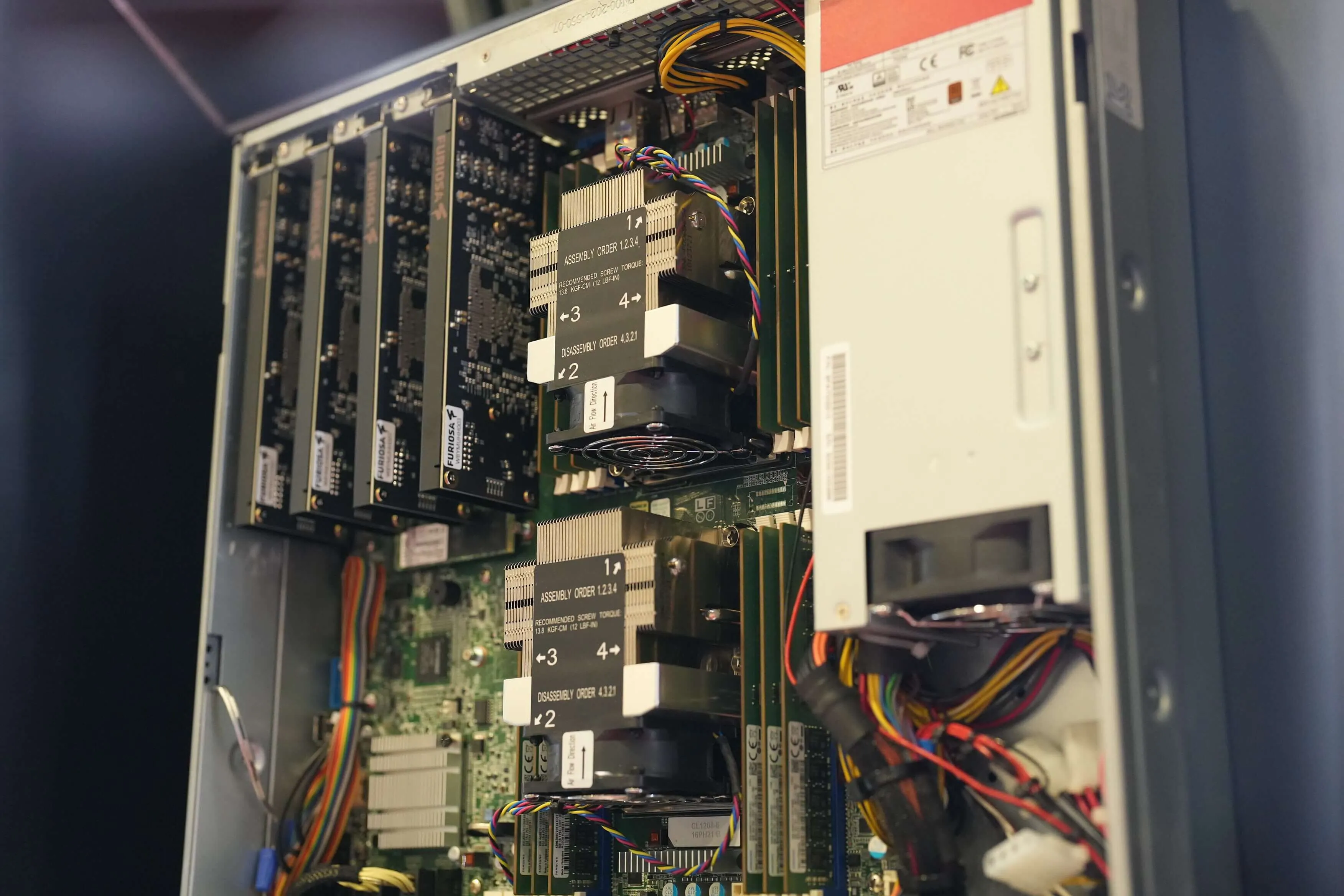 Close-up view inside a server chassis showing multiple accelerator cards installed vertically alongside large heatsinks, cooling fans, memory modules, and bundled power cables. The image highlights the internal hardware layout of a high-performance AI computing system designed for intensive workloads.