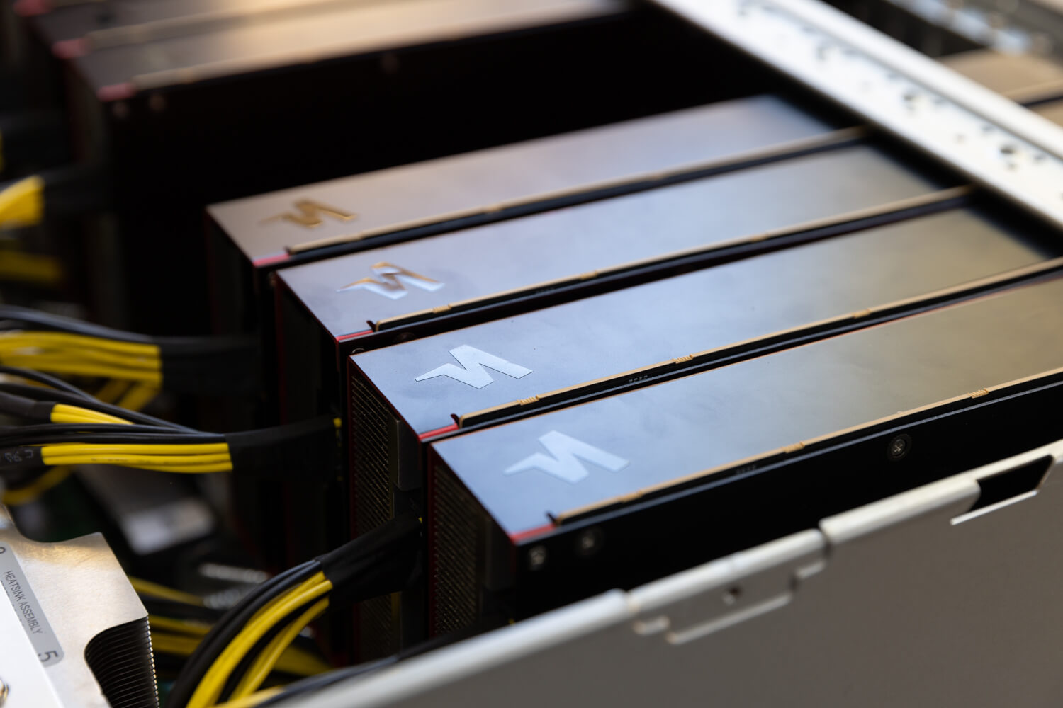 Close-up of multiple Furiosa AI accelerator cards installed in a server chassis, showing metal housings with Furiosa lightning logos and connected power cables inside a data center or demo server setup.