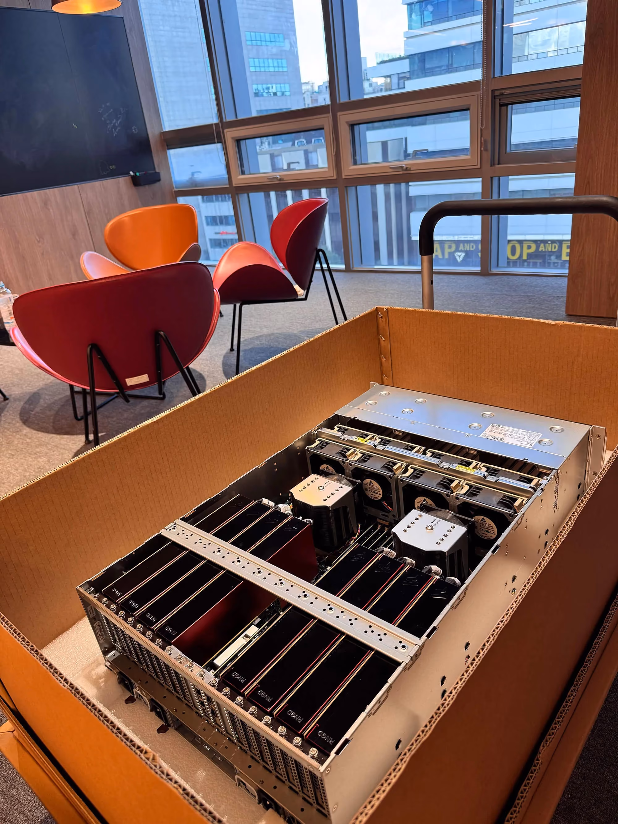 Open shipping crate containing a server system populated with multiple Furiosa RNGD accelerator cards inside an office environment.
