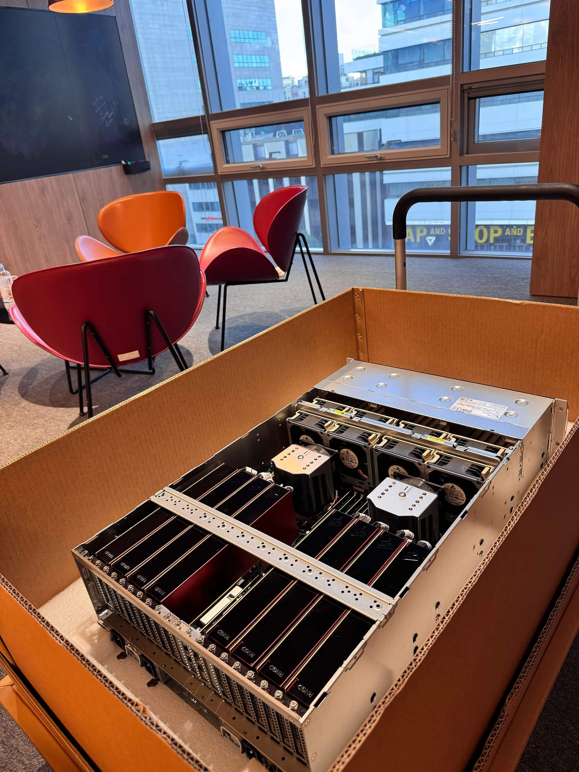 Open shipping crate containing a server system populated with multiple Furiosa RNGD accelerator cards inside an office environment.