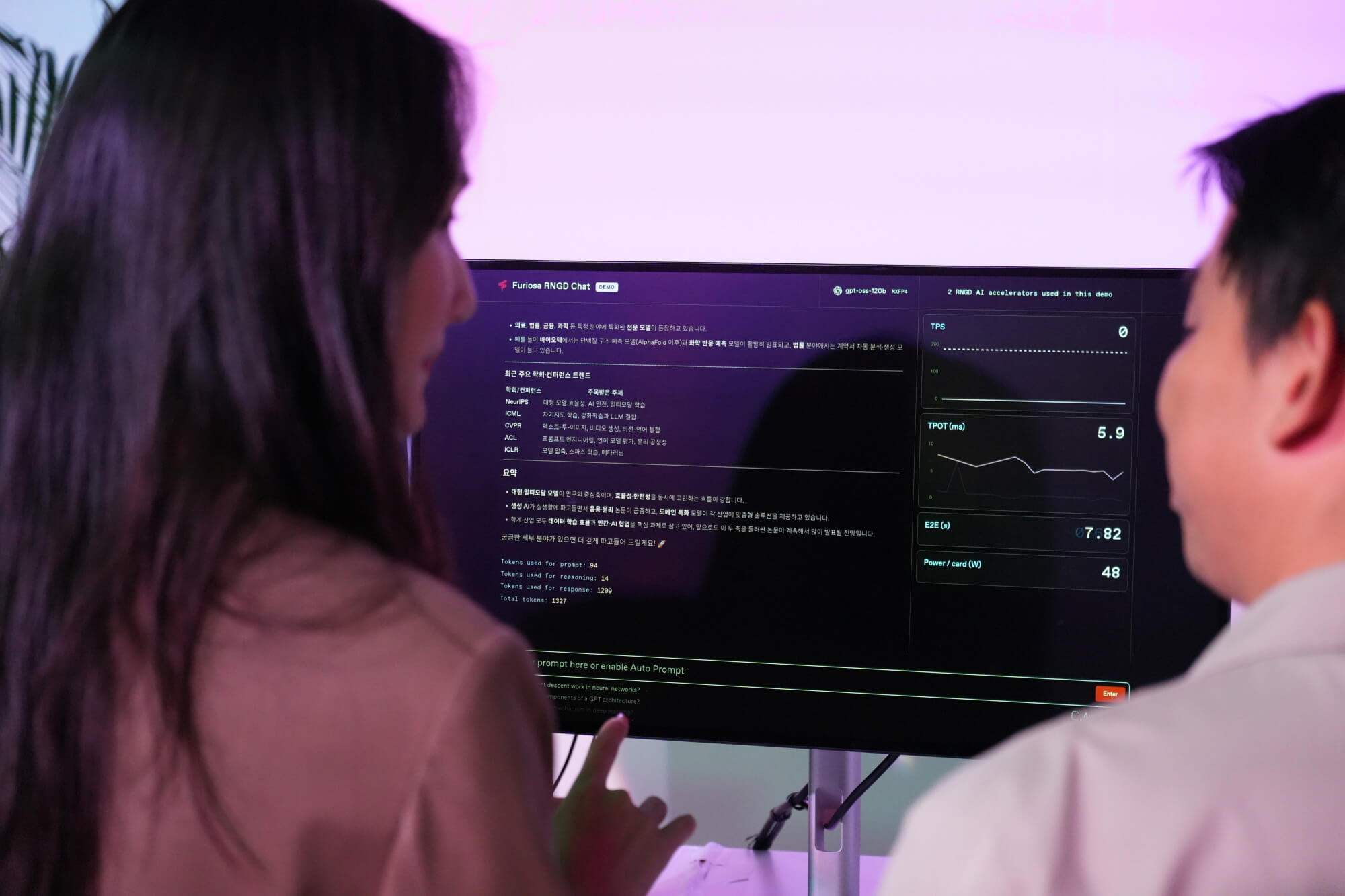 Two people reviewing a live Furiosa RNGD chat demo on a monitor displaying AI inference metrics and performance graphs.