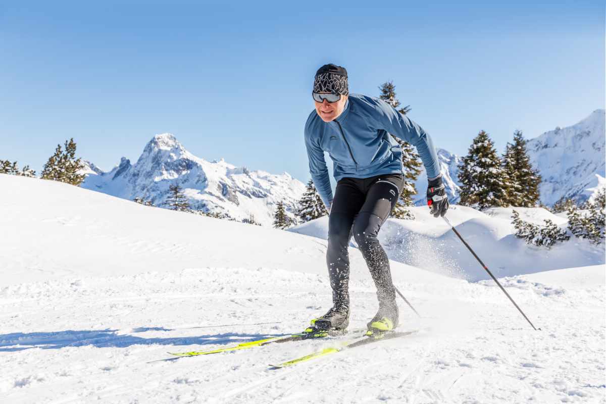 Ein Mann beim Skilanglauf auf einer verschneiten Berglandschaft bei strahlend blauem Himmel.