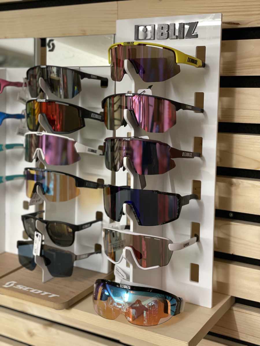 Mehrere Sportsonnenbrillen verschiedener Marken, darunter Bliz und Uvex, in einem Ladendisplay aus Holz und Kunststoff.