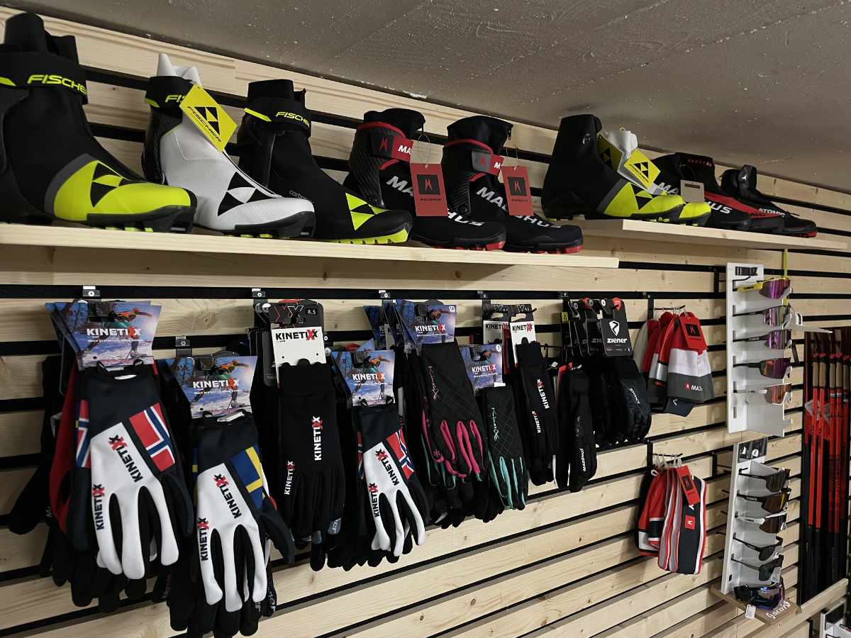 Regal mit Langlaufschuhen in Schwarz, Gelb und Weiß sowie verschiedenen Ski-Handschuhen und Skibrillen.