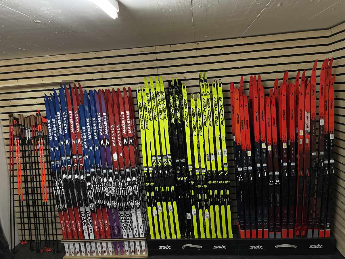 Wandhalter mit mehreren Paaren farblich sortierter Langlaufskier und Skistöcke in einem hellen Raum.