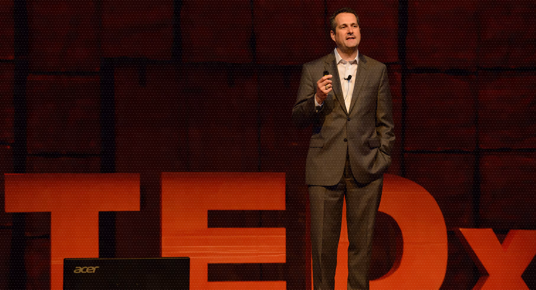 James H. Lee delivering a TEDx talk on stage with large red TEDx letters behind him.
