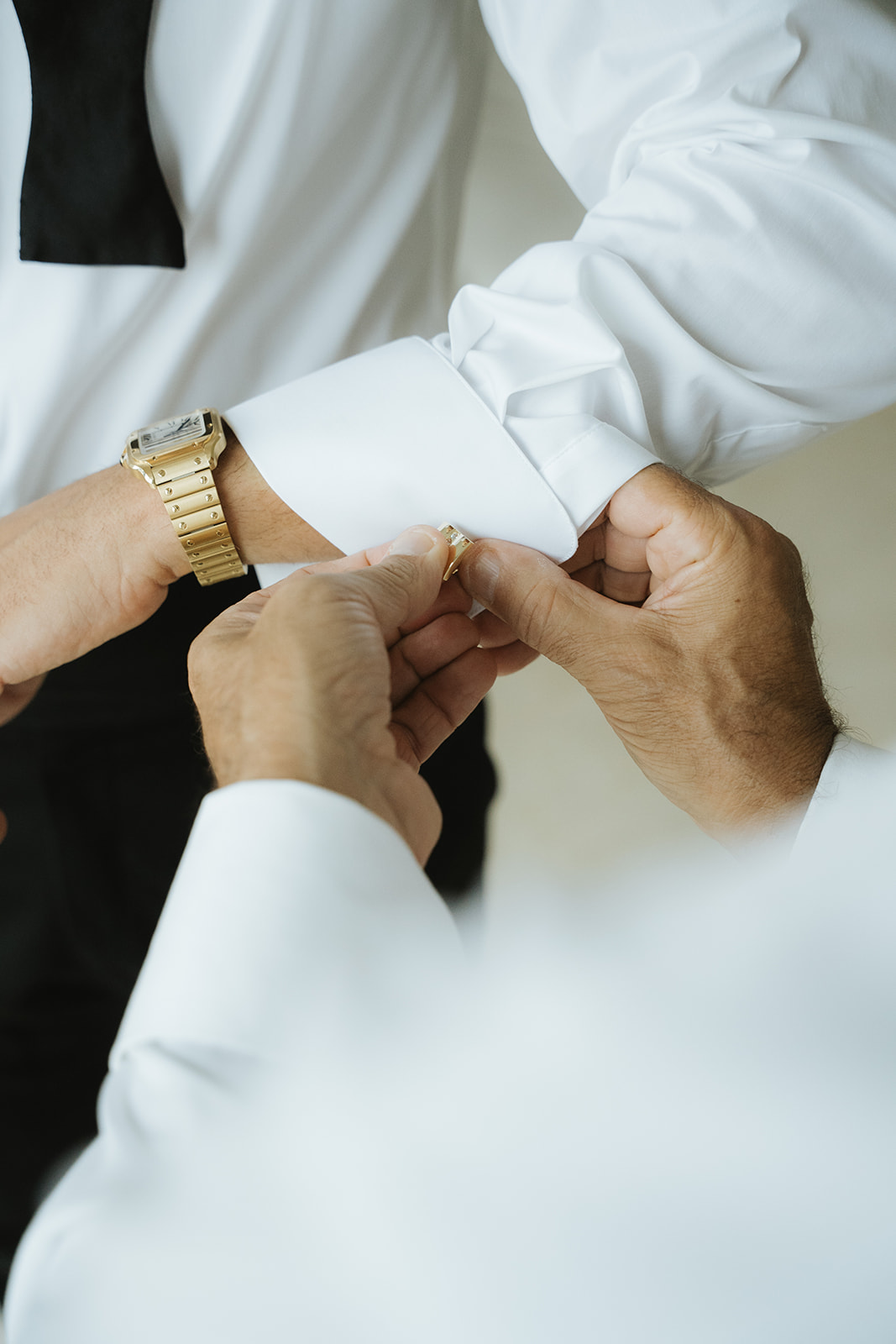 Close-up of a person fastening a gold cufflink on another person’s white dress shirt cuff.