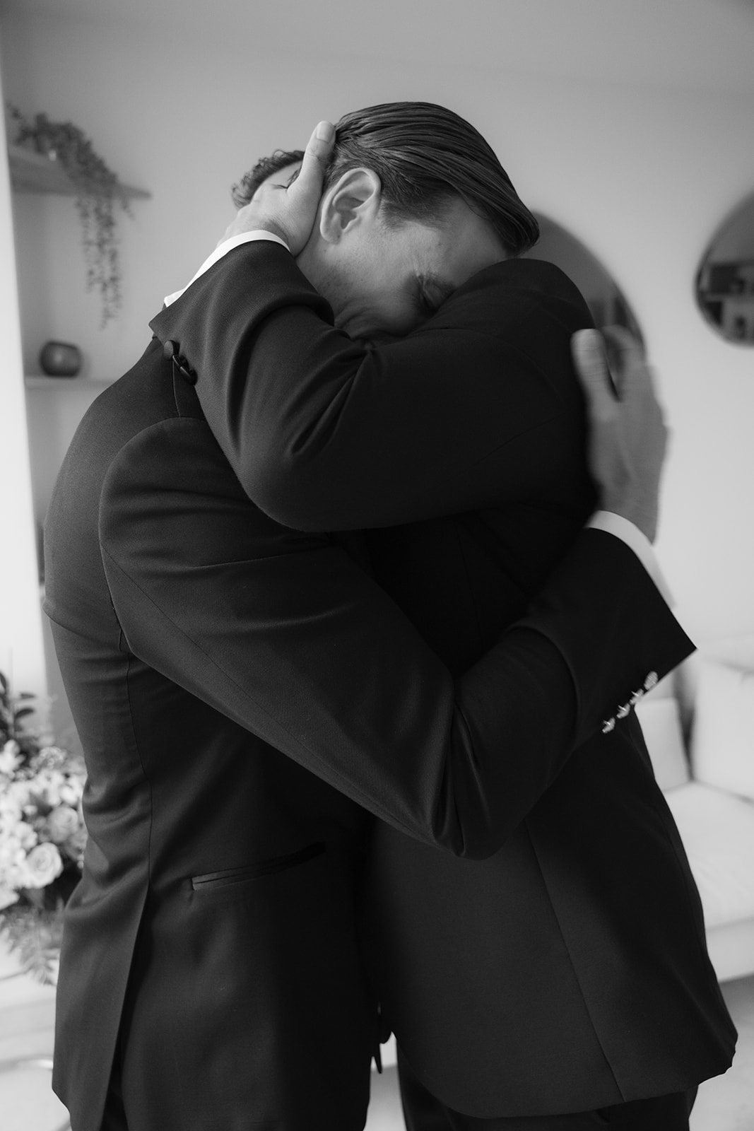 Two men in suits sharing an emotional embrace indoors.